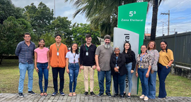 Grupo de onze pessoas em pé, lado a lado, posando para a foto em frente a uma placa verde e cinz...