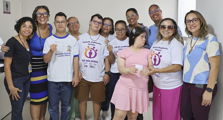 Grupo de dez pessoas posa em ambiente interno claro, sorrindo e próximas umas das outras. Entre ...