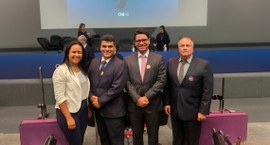 Fotografia em ambiente de auditório mostra quatro pessoas em pé, lado a lado, posando para a câm...