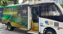 Ônibus do projeto “TRE Aqui”, nas cores verde, amarelo e branco, estacionado ao ar livre. A port...