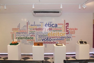 Foto da parte interna do CEMEL que contém quatro móveis brancos em formato de cubo, com cópia de...